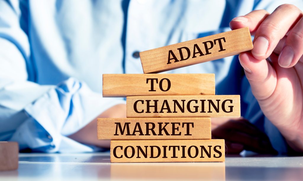 A hand places wooden blocks reading "Adapt to Changing Market Conditions," symbolizing strategic flexibility in business.